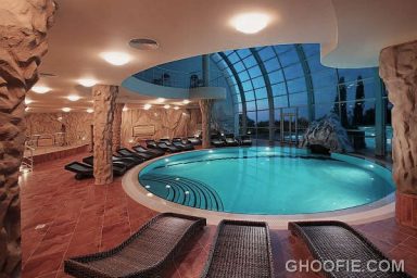 Fabulous Rounded Indoor Swimming Pool Design with Rattan Lounge Chairs